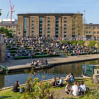 people sitting on the grass next to a canal