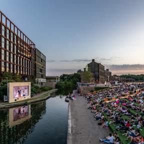 people watching a movie along the canal at sunset