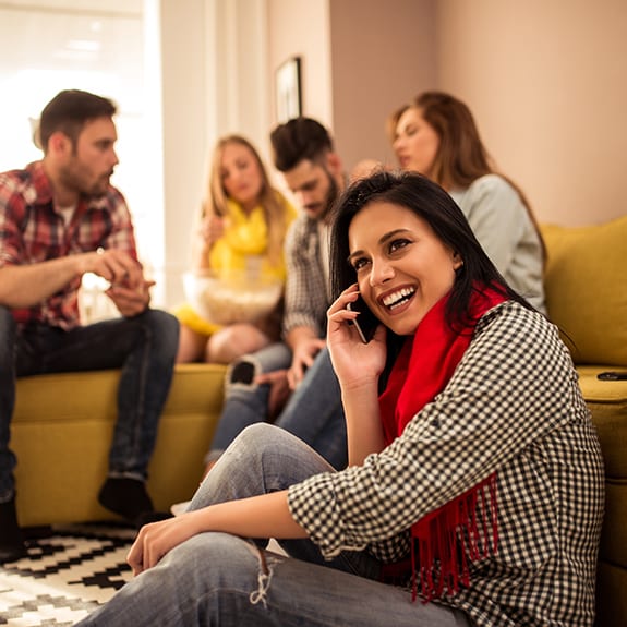 a woman on the phone in a living room with a group of people in the background