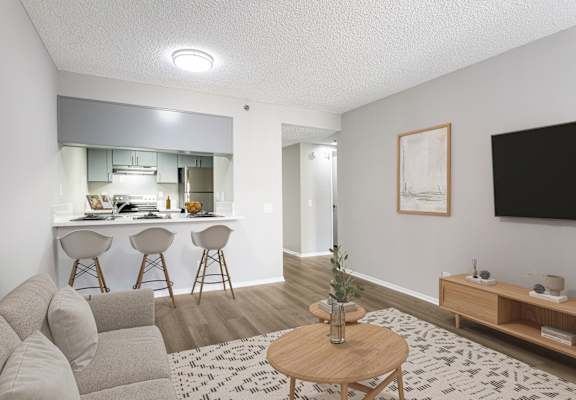 A living room with a grey couch, a wooden coffee table, and a kitchen area in the background.