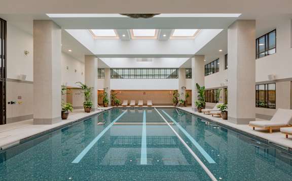 A large indoor swimming pool with lounge chairs and plants.