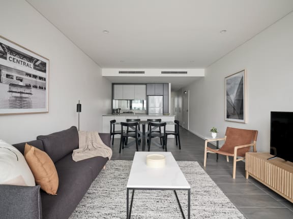 a living room with a couch and a coffee table and a kitchen in the background