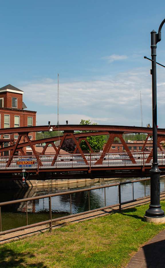 A bridge over a river with a building in the background. at Highview Manor Apartments, New York, 14450
