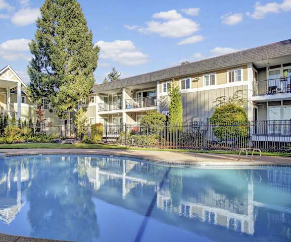 Outdoor pool with an attached hot tub The turquoise outdoor pool with pool chairs, tables, and chairs with the apartments in the background at Regency Woods Apartment Homes.