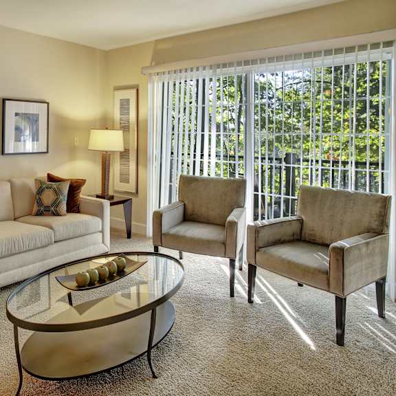 The living room with a couch, plush chairs, coffee table, decorations, a TV, and balcony at Regency Woods Apartment Homes.