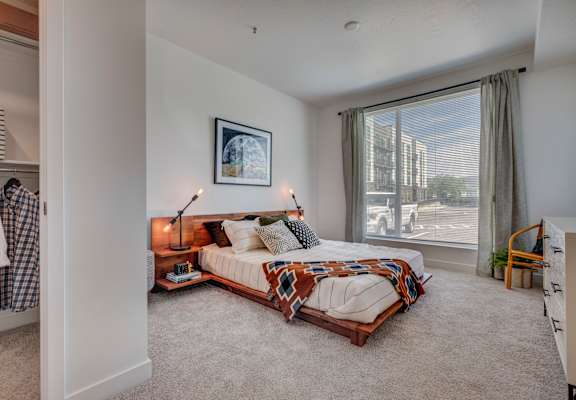 A bedroom with a bed, a chair, and a window overlooking a street.