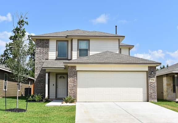 A two-story house with a garage door and a tree in front.