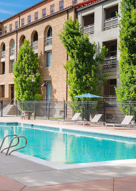 A pool surrounded by lounge chairs and trees.