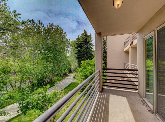 A balcony with a metal railing overlooks a tree-lined road. at River Walk Apartments, Boise