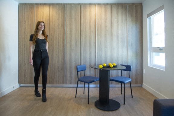 a woman standing in a room with a table and chairs