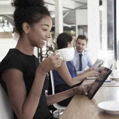 A woman is drinking coffee while using a tablet in a cafe.