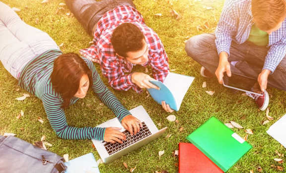 Three people are sitting on the grass with laptops and notebooks.