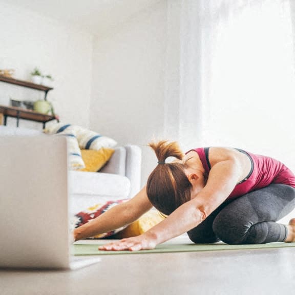 a woman doing yoga on the floor in front of a laptop computer