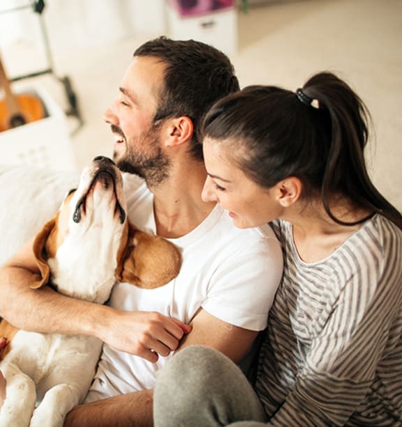 A man and woman are sitting on a couch with a dog between them.