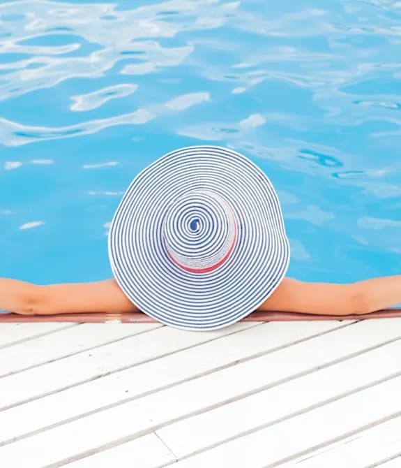 A person wearing a striped hat is sunbathing by the pool.