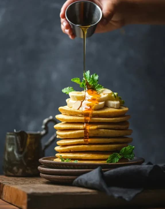 A person is pouring syrup on a stack of pancakes.