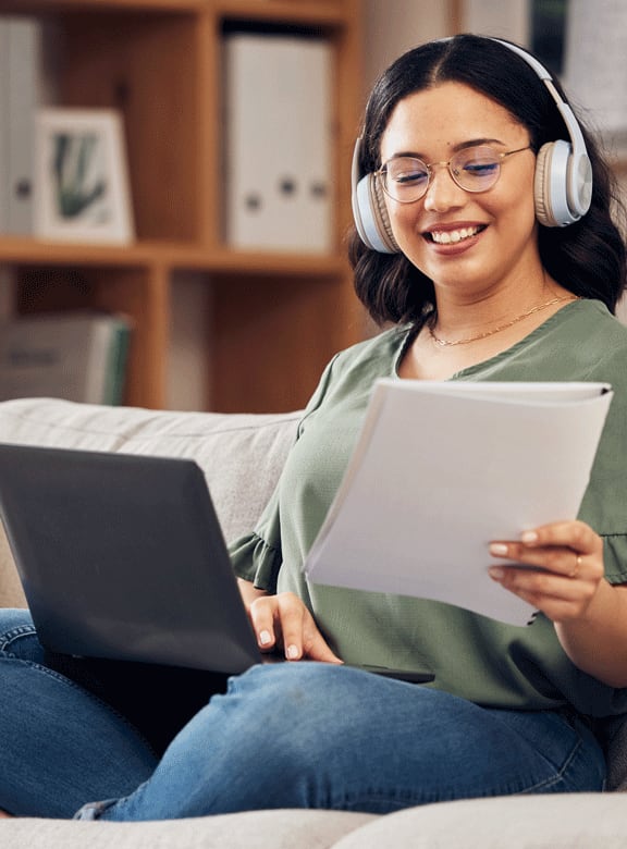 Lifestyle photo of a woman smiling holding a piece of paper with her computer on the couch