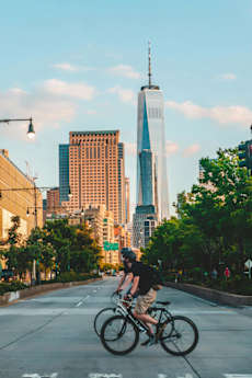 A man riding a bike on a city street with tall buildings in the background.
