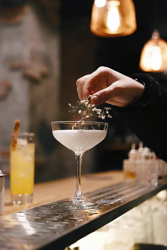 A person is sprinkling something into a glass of a cocktail.