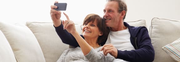 an older couple sitting on a couch taking a picture of themselves with their cell phone 
