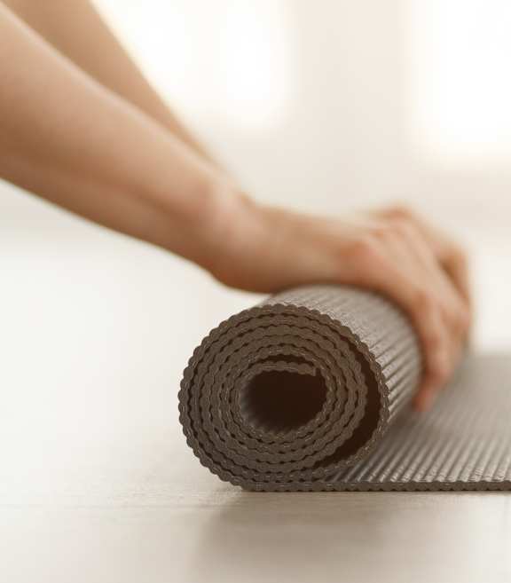 A person is rolling up a brown yoga mat.