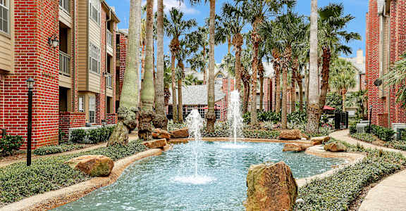 a fountain in the middle of a pool with palm trees