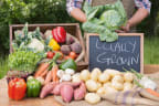 a person holding a bag of lettuce next to a pile of vegetables on a table with a