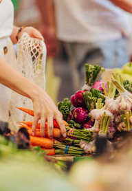 A woman in a white dress is shopping for vegetables at a market.