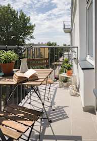 A balcony with a table, chairs, and a potted plant.