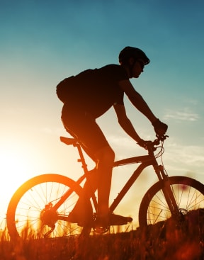 a man riding a bike on a hill at sunset