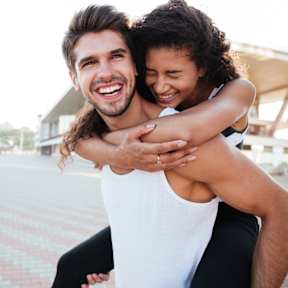 A man in a white tank top is giving a woman a piggyback ride.