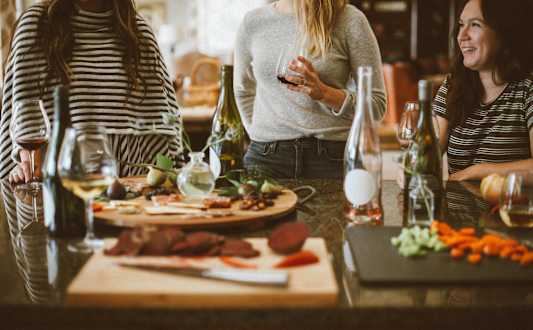 Three women are sitting at a table with wine glasses and food.