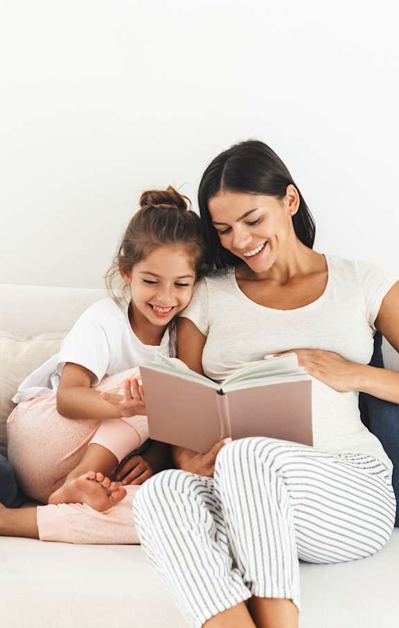 Two people are sitting on a couch, one is reading a book to the other.