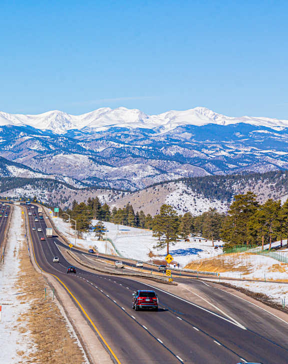 A highway with cars driving on it and snow covered mountains in the background.