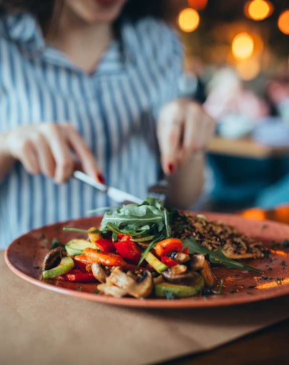 A woman is cutting a salad on a plate.