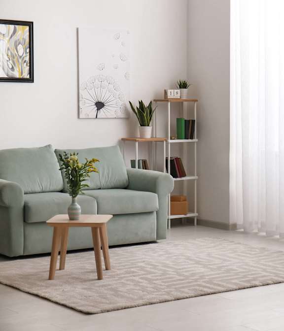 A living room with a green couch, a wooden table, and a painting on the wall.