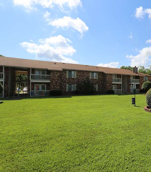 A grassy courtyard in front of a building with a bush in the middle.
