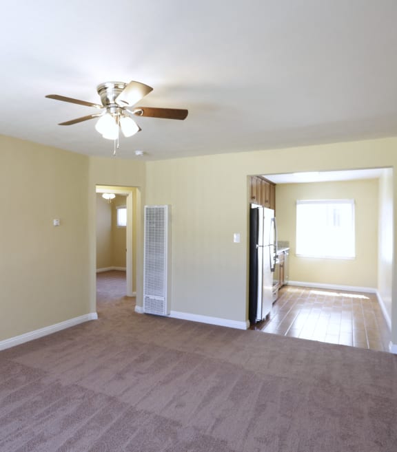 a empty living room with a ceiling fan and a kitchen