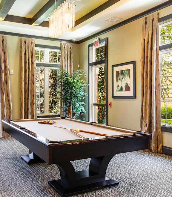 A pool table in a room with large windows and curtains.