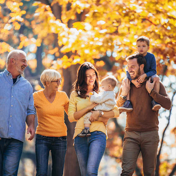 A family of four walking in a park with trees showing autumn leaves.