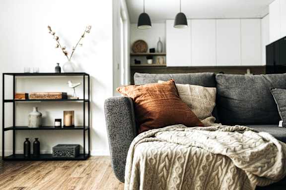 A grey couch with a blanket and pillows in a room with a shelf and decorations.