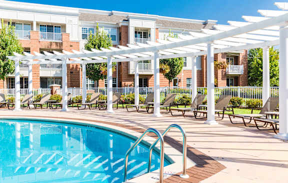 A swimming pool is surrounded by chairs and a white pergola.