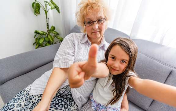 An older woman and a younger girl are sitting on a couch looking at a tablet.