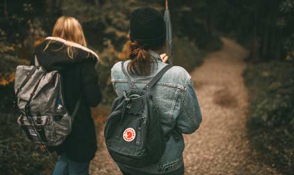 A woman and a child are walking together on a path in a natural setting.