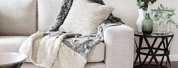 A grey couch with a blanket on it.