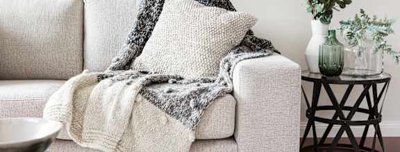 A grey couch with a blanket on it.