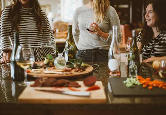 Three women are sitting at a table with wine glasses and food.