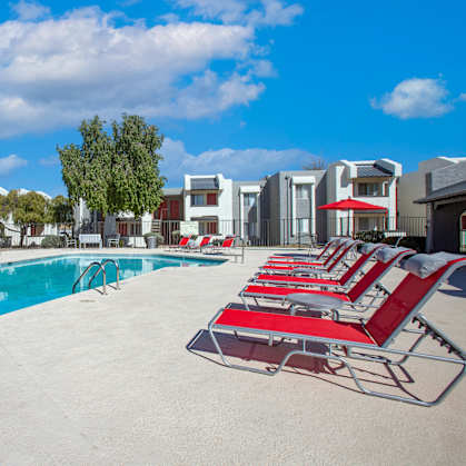a swimming pool with red chaise lounge chairs and apartment buildings in the background