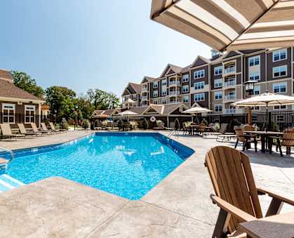 A large swimming pool with a wooden chair and umbrella.