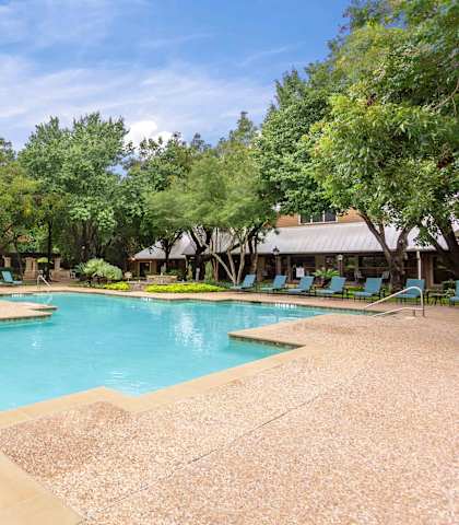 A large swimming pool surrounded by trees and lounge chairs at Ventana Oaks Apartments, Texas